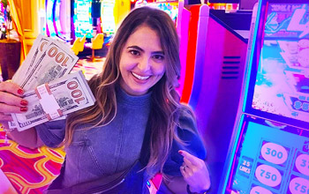 Foto von Francine Marin alias Lady Luck HQ, die Stapel von Dollarscheinen in der Hand hält und neben einem Spielautomaten steht. 